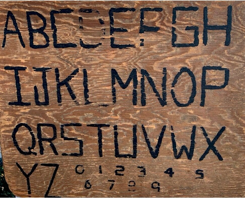 Bob’s first communication board: a piece of brown wood handprinted with the alphabet in capital letters and the numerals 0 through 9.