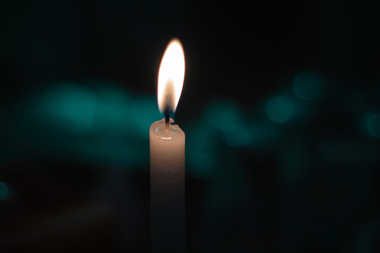[image description: A peach-colored candle is lit against a black and aqua mottled backdrop]