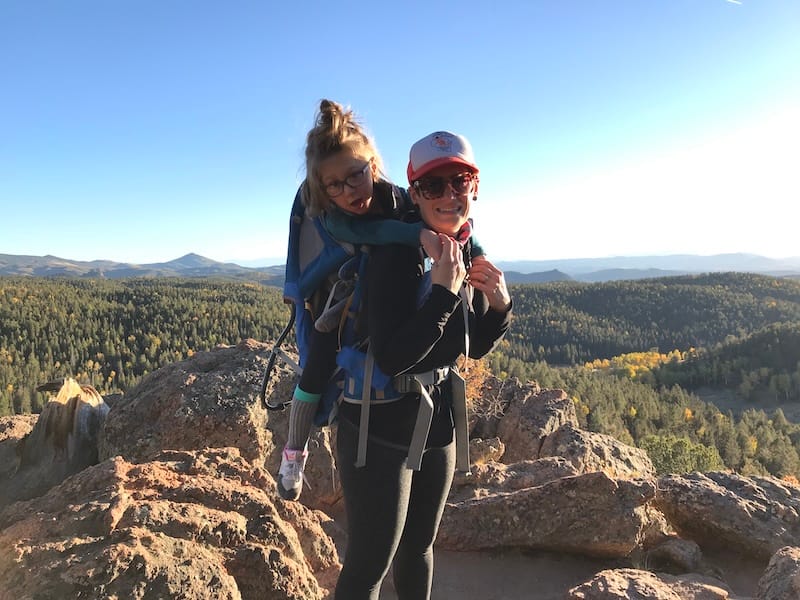 Olive in a carrier on her mom's back at the top of a mountain.
