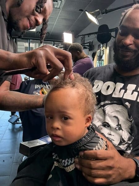 A worried-looking Black toddler getting a haircut.