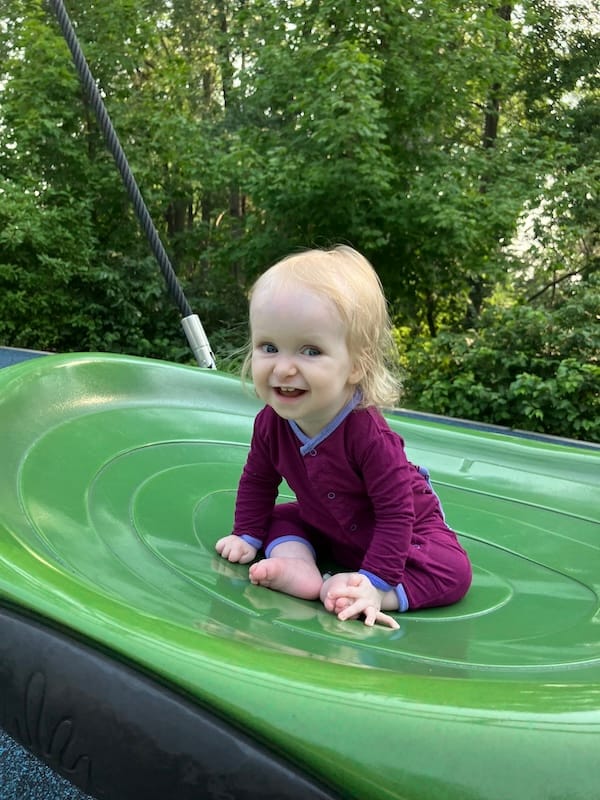 A blonde child with a gap-toothed grin and bright eyes wearing a maroon onesie.