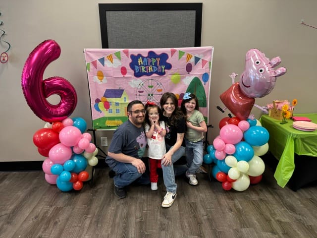 Kinsley and her family beaming in front of sixth birthday decorations.