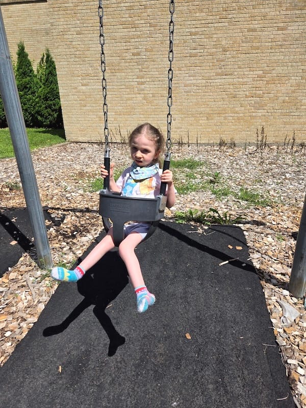 A smiling blonde child on a swing.