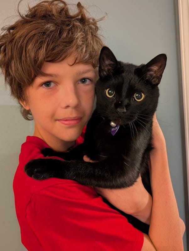 A smiling white boy holding a black cat.