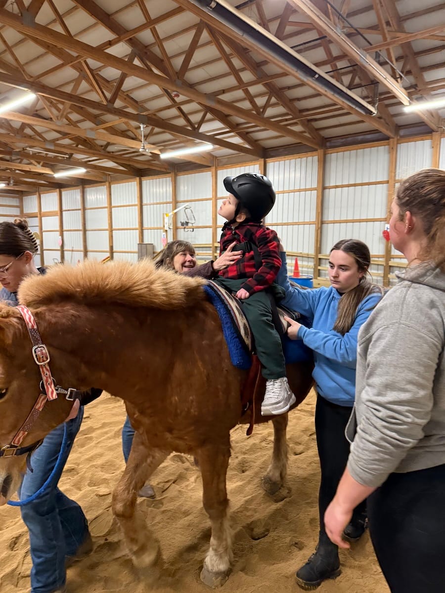 Theo riding Sherman in an indoor arena, surrounded by assistants.