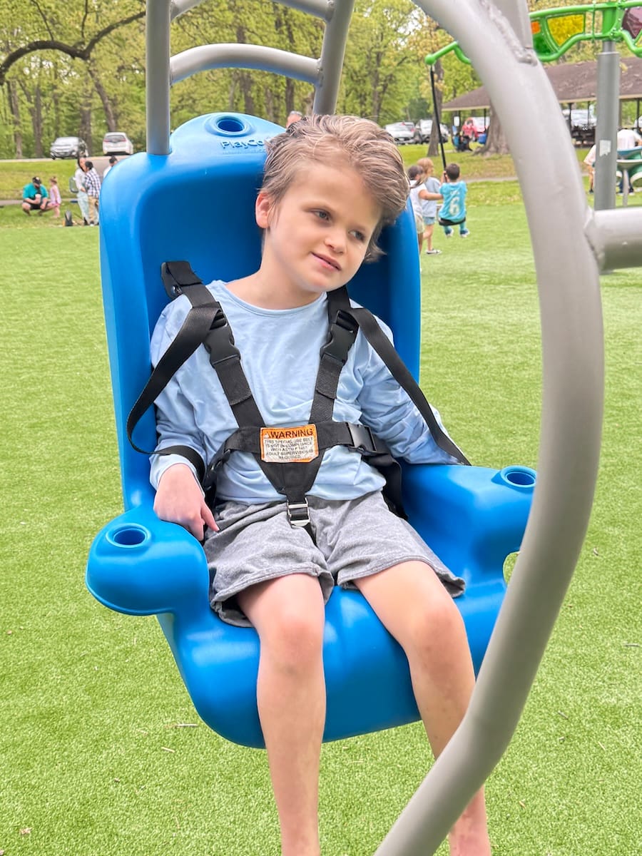 Theo in a blue adaptive swing at the playground.