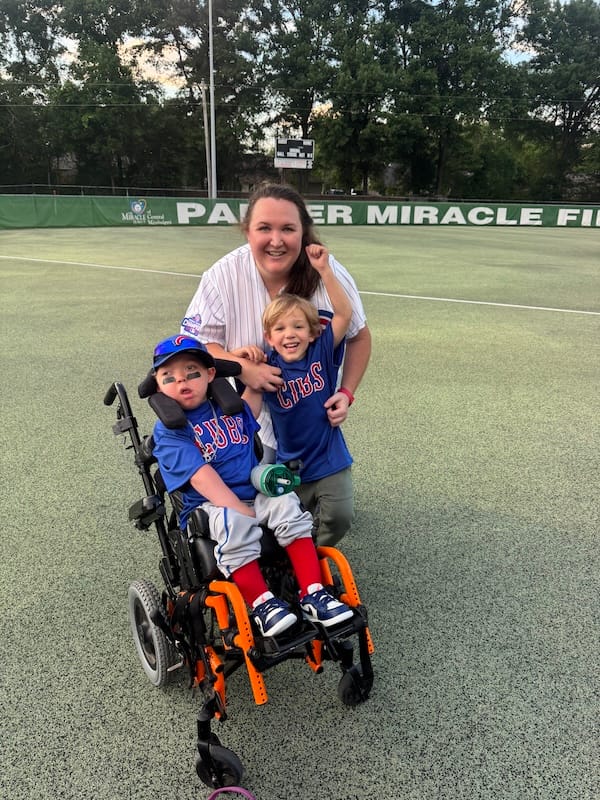 Peter and Zachary in Cubs gear at a ballgame with Lisa. Peter is seated in his wheelchair and beaming, while Zachary wiggles with joy.
