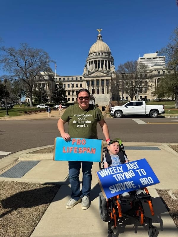 Lisa and Peter holding up signs: Pro Lifespan and Wheely Just Trying to Survive, Bro.
