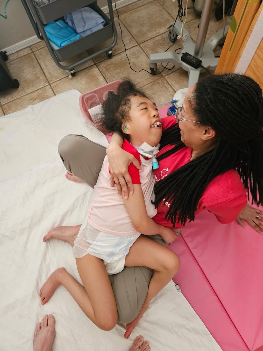 Dianne, a Black woman with long hair, cradling Madison in bed. Both are smiling.