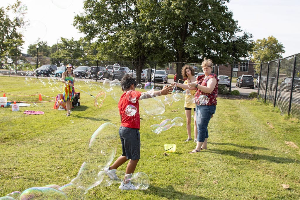 Kids and adults play with giant bubbles in a grassy yard.