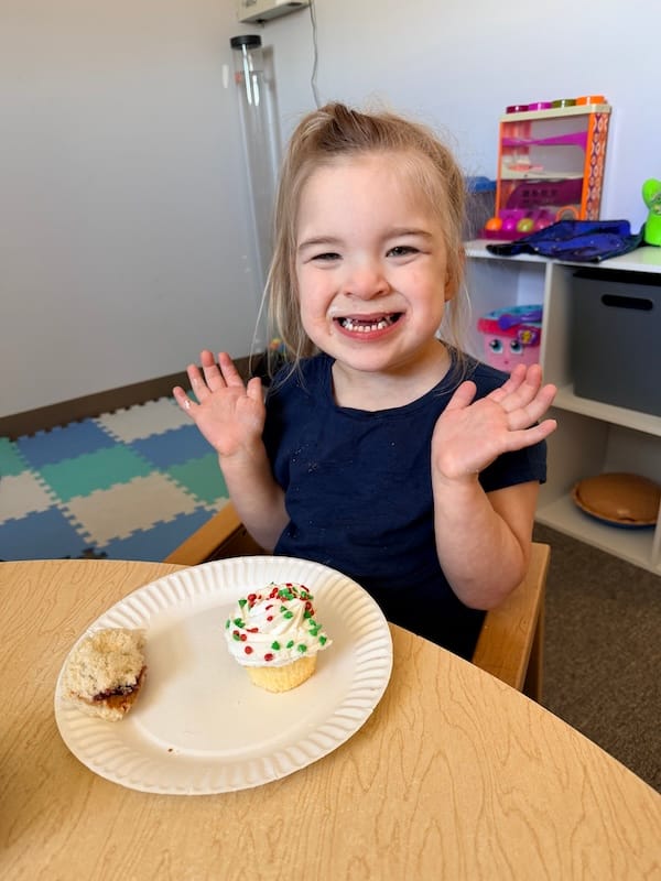 Violette seated at a table with a plate containing a cupcake and peanut butter and jelly sandwich.
