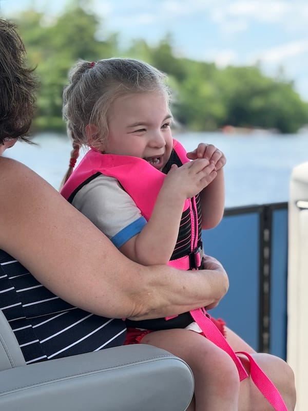 Violette, wearing a hot-pink life vest, sitting on her mom's lap.