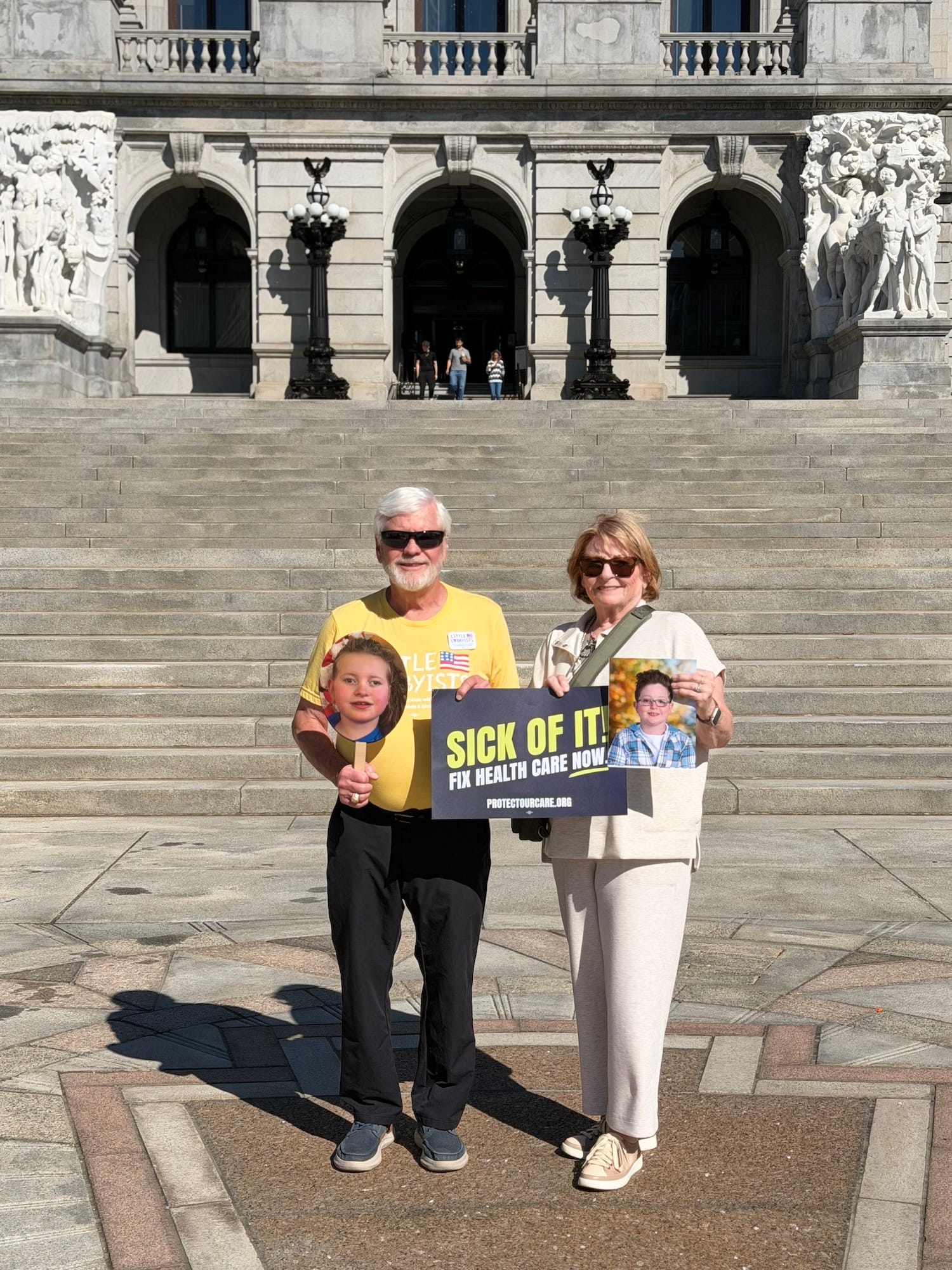 Two older white adults holding up photographs of Victoria's son Cole and Chelsea's daughter Olivia.