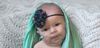 A baby wearing an oxygen cannula, a floral headband, and a soft green scarf.