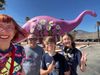 The McLelland family beaming in front of a giant purple dinosaur covered in flowers.