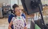Madison, a biracial child with her hair in a ponytail, sits in her wheelchair with a big grin.