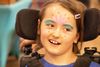 Mira Crump in her wheelchair smiling with a fun summery design painted on her face.