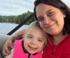 A white woman with mid-length brown hair hugs her smiling blonde daughter. They're on a boat on a lake and Violette wears a hot-pink lifejacket.