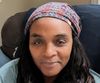A Black woman with a paisley headscarf and long hair, lips curved up in a smile. 