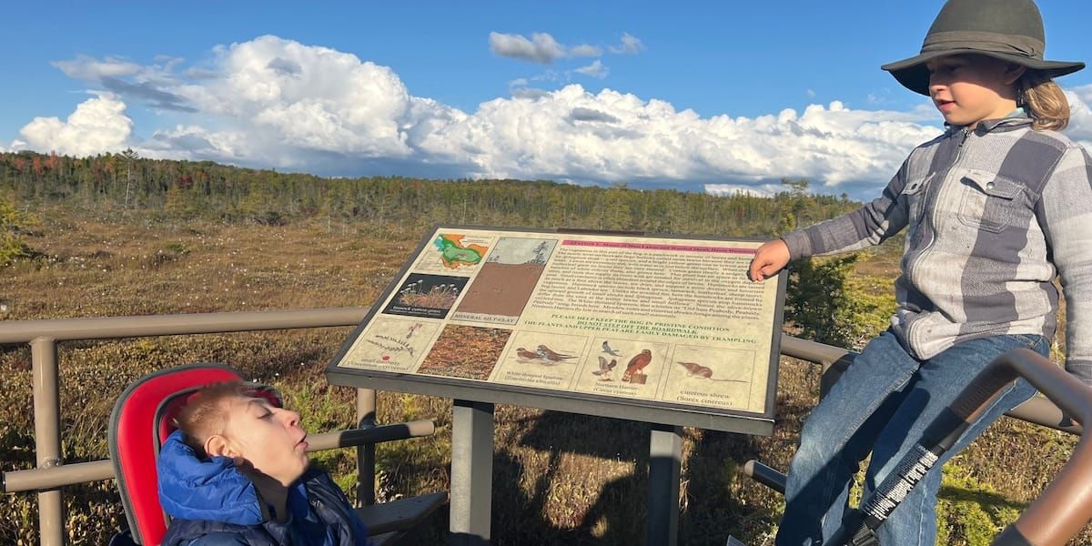 James in a wheelchair smiling up at his brother Rafe. The Orono bog expands behind them in the background.