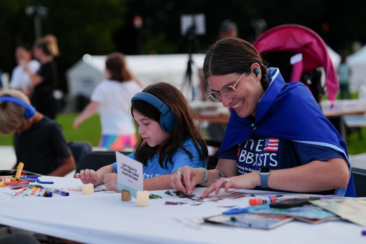 A smiling parent next to their child, making collages at a Protect Medicaid Summer event.