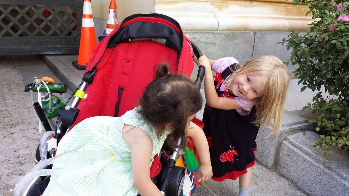 Two young children, one in a medical stroller, playing together.