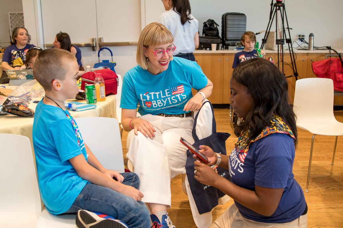 Three smiling people in Little Lobbyists shirts sitting at a table.