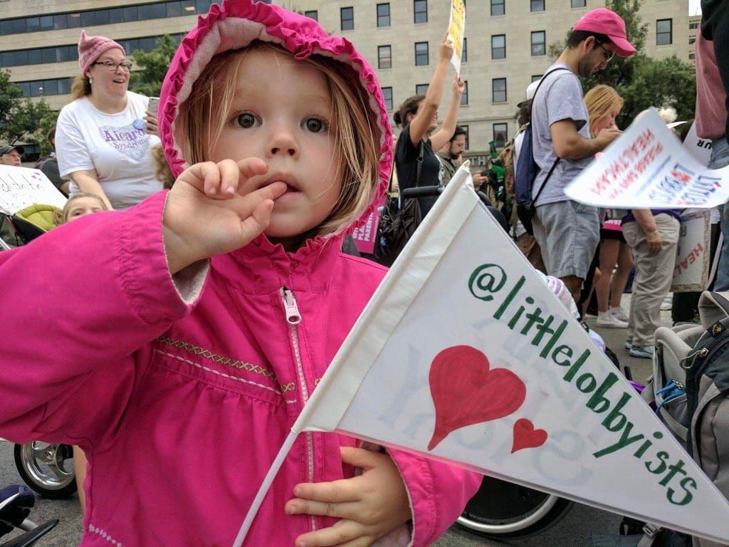 A child in a pink puffer jacket waving a Little Lobbyists flag.
