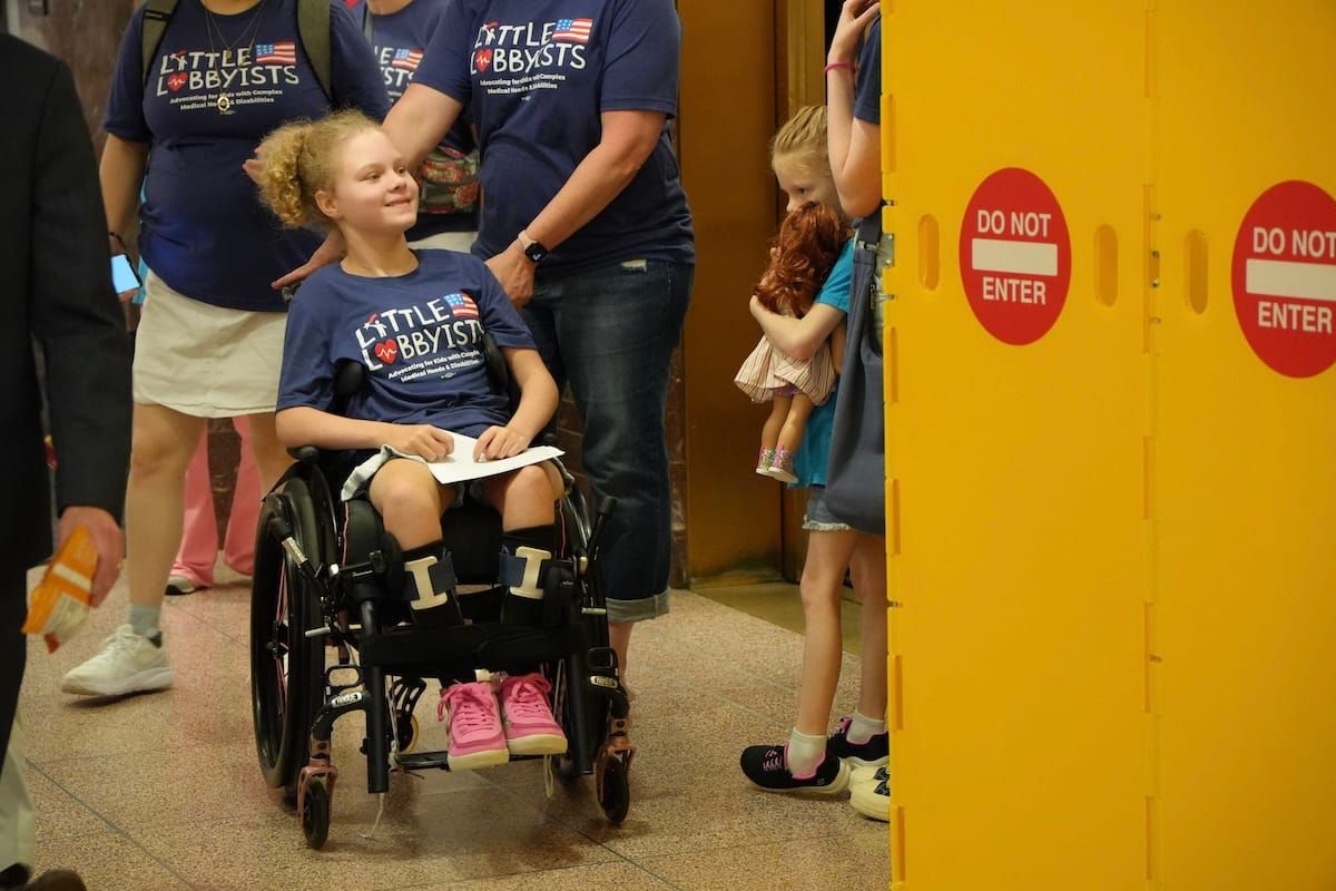 A child in a Little Lobbyists shirt wheeling past barriers that say "do not enter."