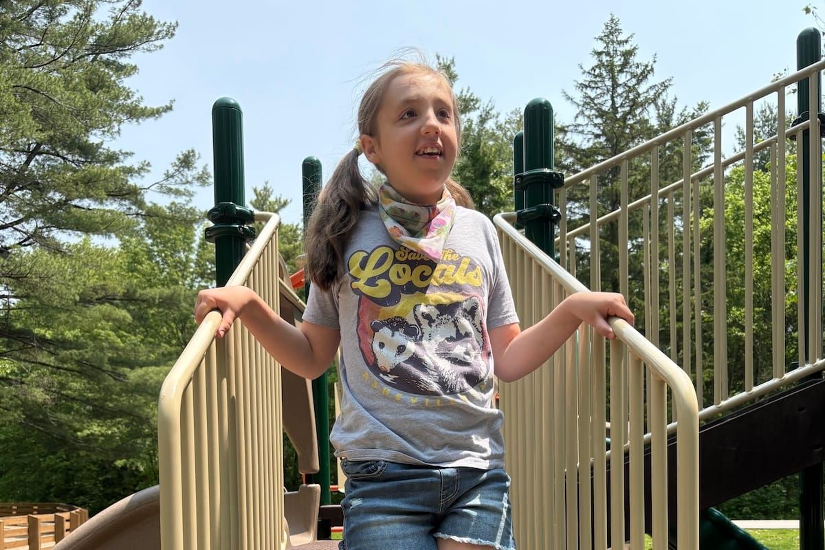 Audrey Anderson smiling broadly while standing on a playground structure. 