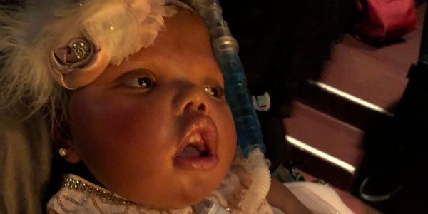 Ansley, a biracial child wearing clothes fit for a princess with a beautiful floral fascinator, at the ballet.