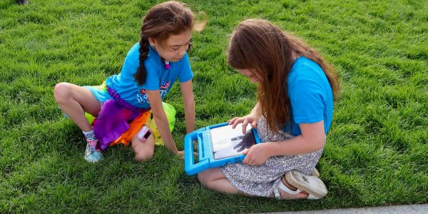 Two children sitting outside and looking at a tablet. 