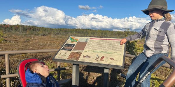 James in a wheelchair smiling up at his brother Rafe. The Orono bog expands behind them in the background.