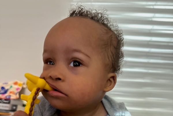 A Black toddler chewing thoughtfully on a teether toy.