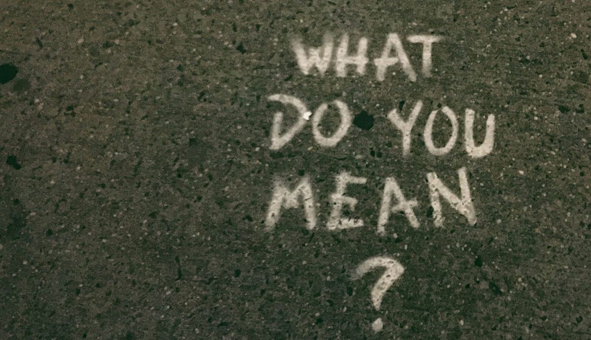 Graffiti on a sidewalk reading "What do you mean?"