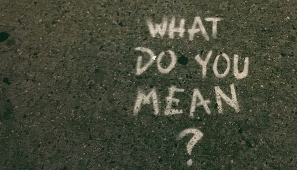 Graffiti on a sidewalk reading "What do you mean?"