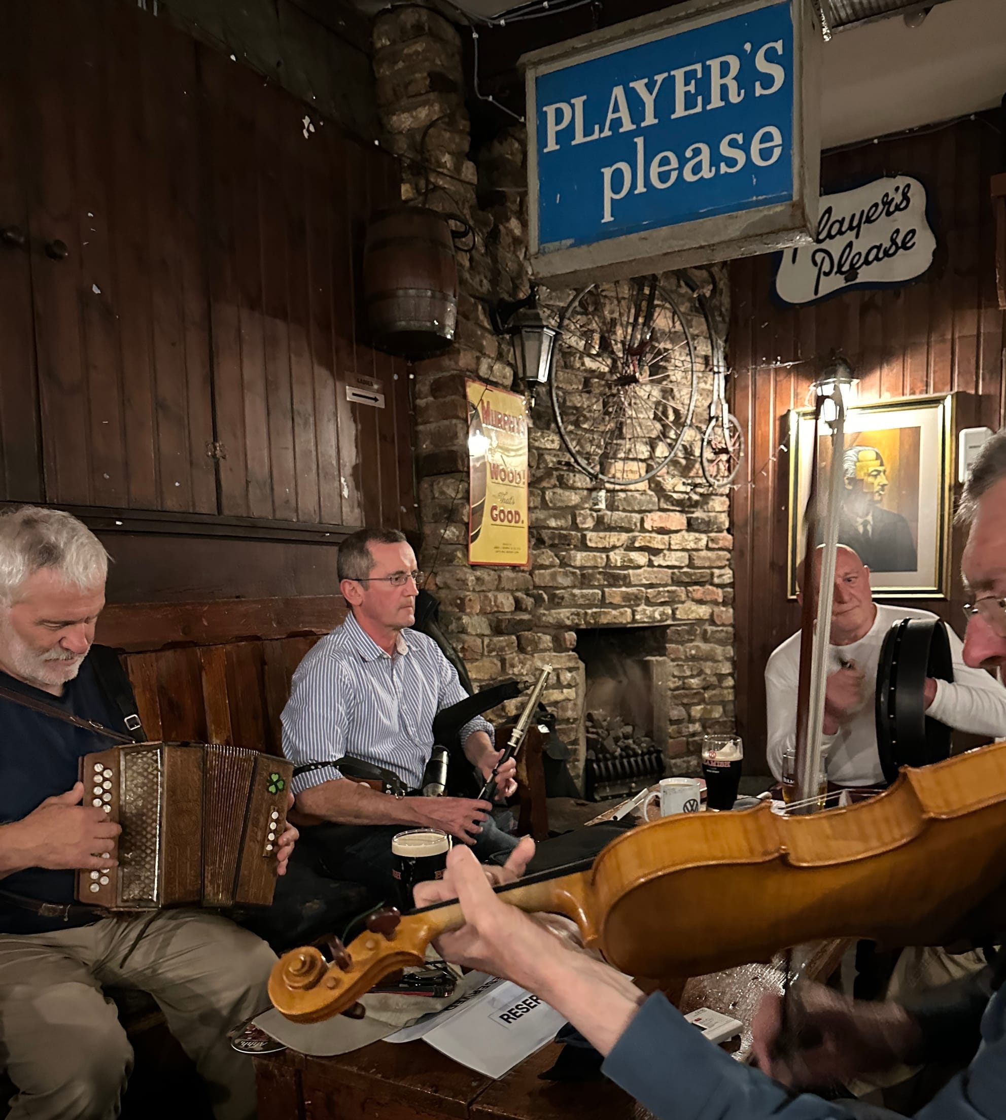 Four musicians gather around the reserved area.  They are play button accordion, uilleann pipes, bodhran, and fiddle. 