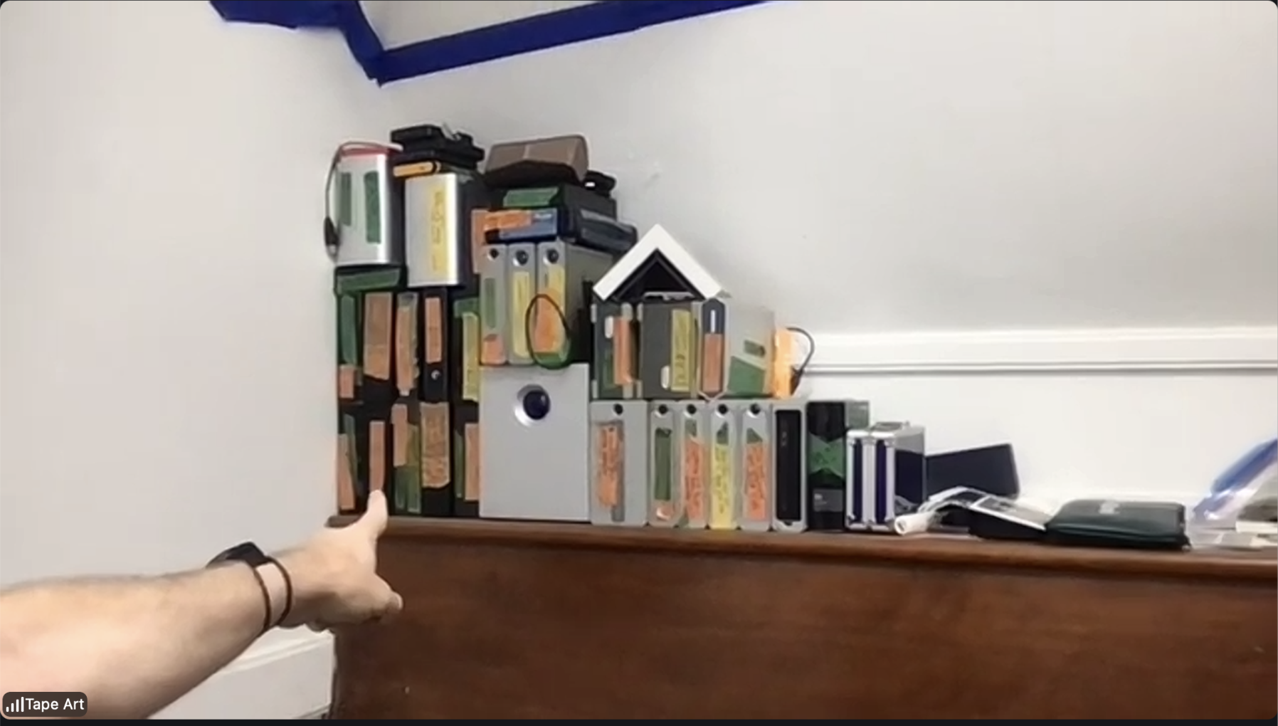 A hand points toward a shelf of old computer equipment in the Tape Art studio during our Zoom call.