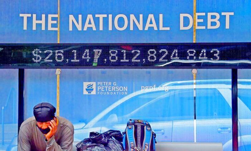 A man waits at a bus stop that displays the official national debt of the United States in Washington on June 19, 2020. The nonprofit Truth in Accounting says the actual national debt is more than four times the official figure. (Olivier Douliery/AFP via Getty Images)
