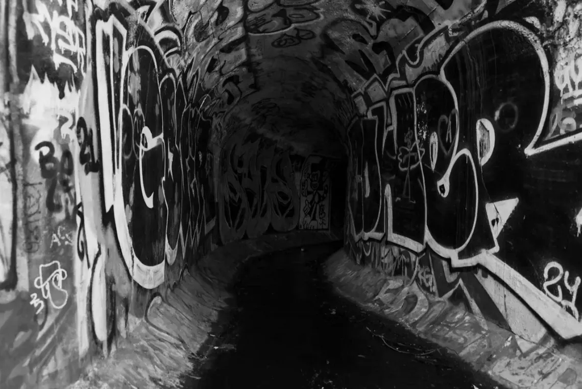 High contrast monochrome photo of a graffiti covered tunnel leading into a distant blackness.