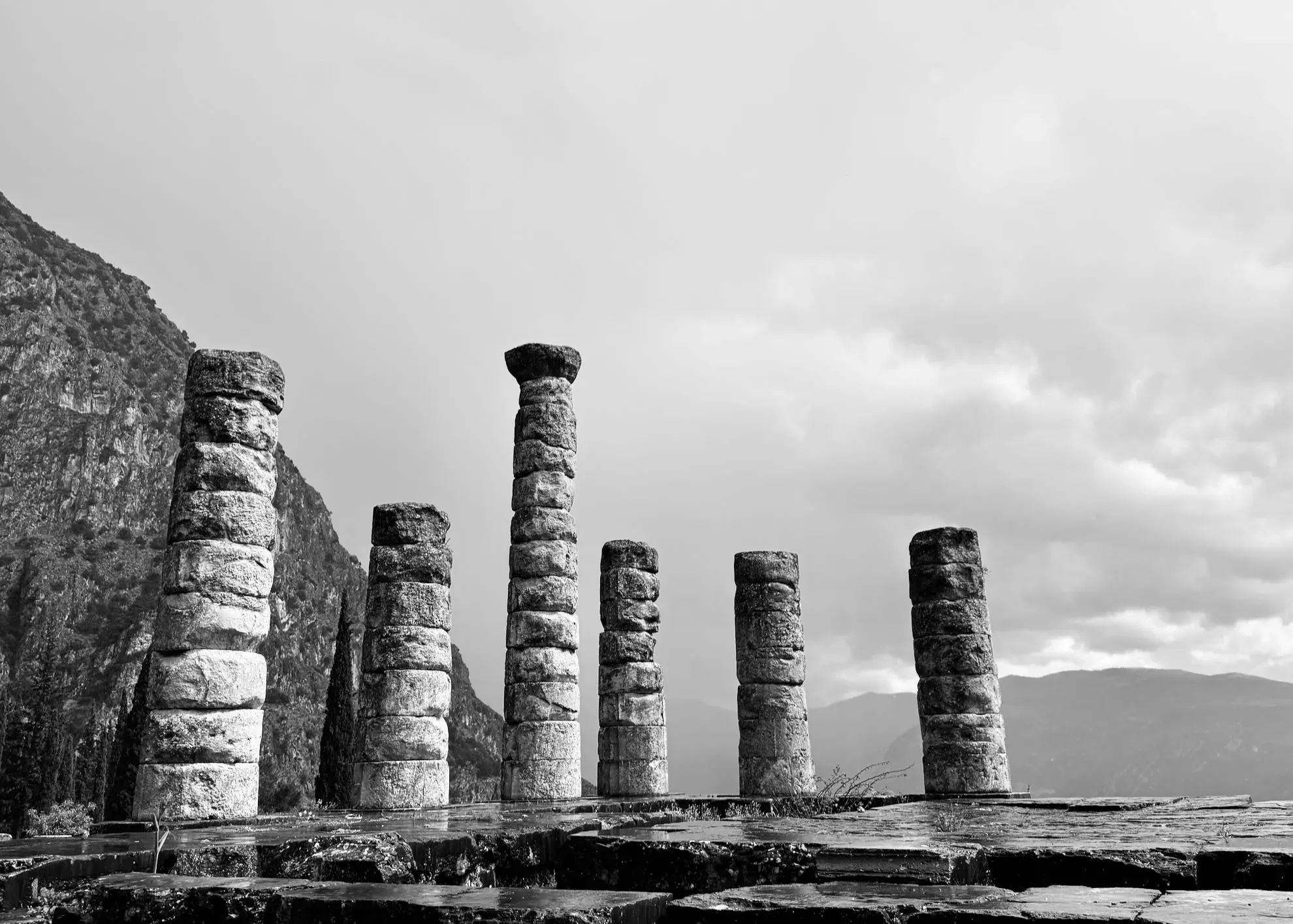 Black and white photograph of ancient stone columns against a dramatic, cloudy sky.