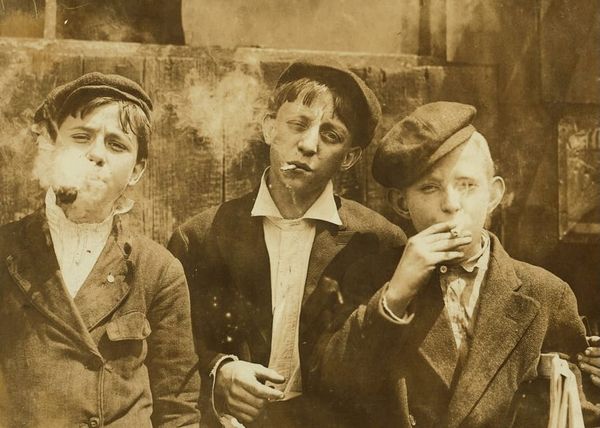 Vintage photo of three young boys from an earlier century defiantly looking at the viewer, while smoking up a storm.
