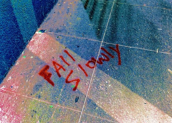 The words, "Fall Slowly," written in spray paint on a sidewalk.