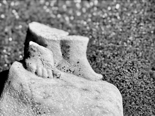 Black and white photograph of tiny concrete feet with a blurred background.
