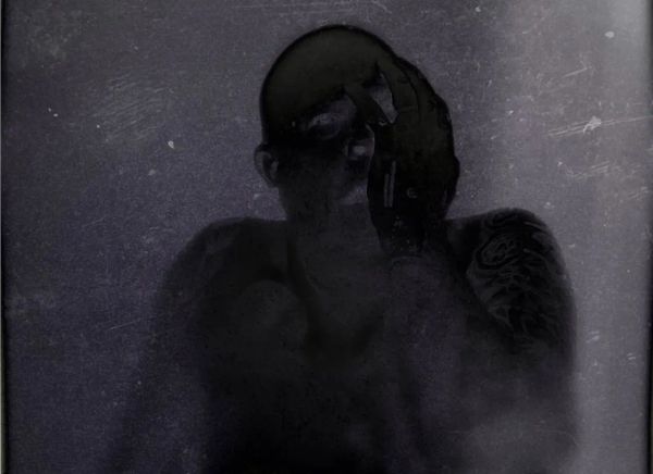 very dark and creepy photo of a man with his hand covering his face