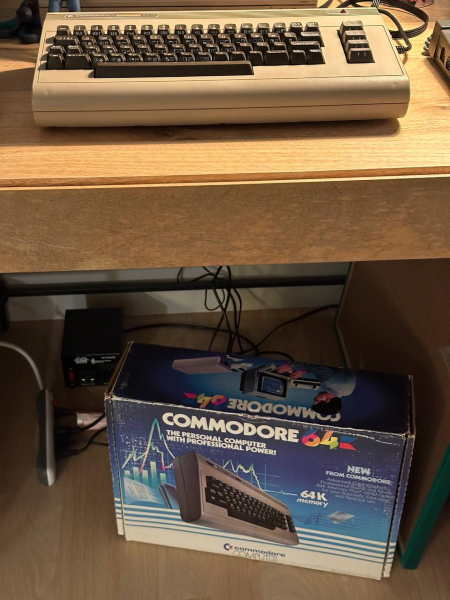 A desk with a Commodore 64 keyboard is on. Under the desk, there is an original box of Commodore 64.