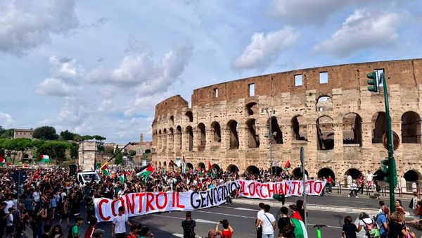 A large crowd of people carrying a banner outside the Colosseum, on the General Strike for Gaza