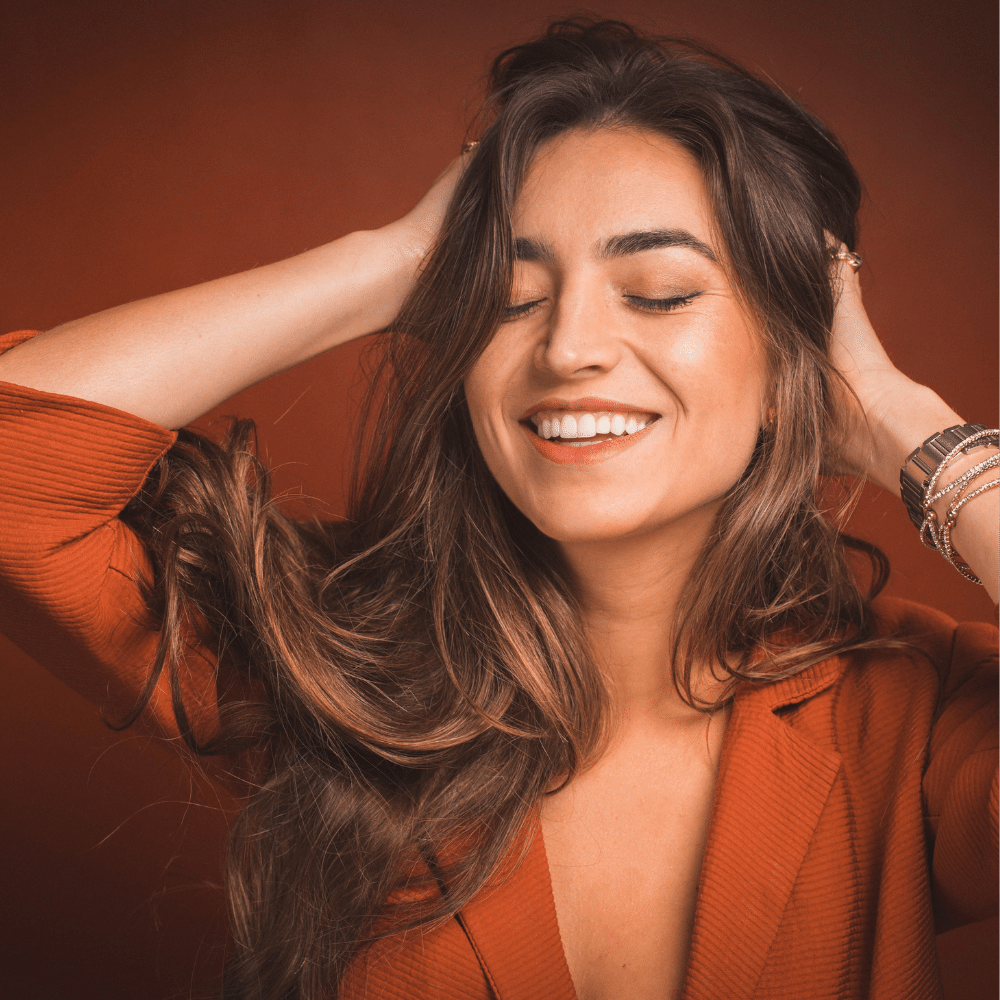 woman touching her long, dark, healthy hair, with a smile