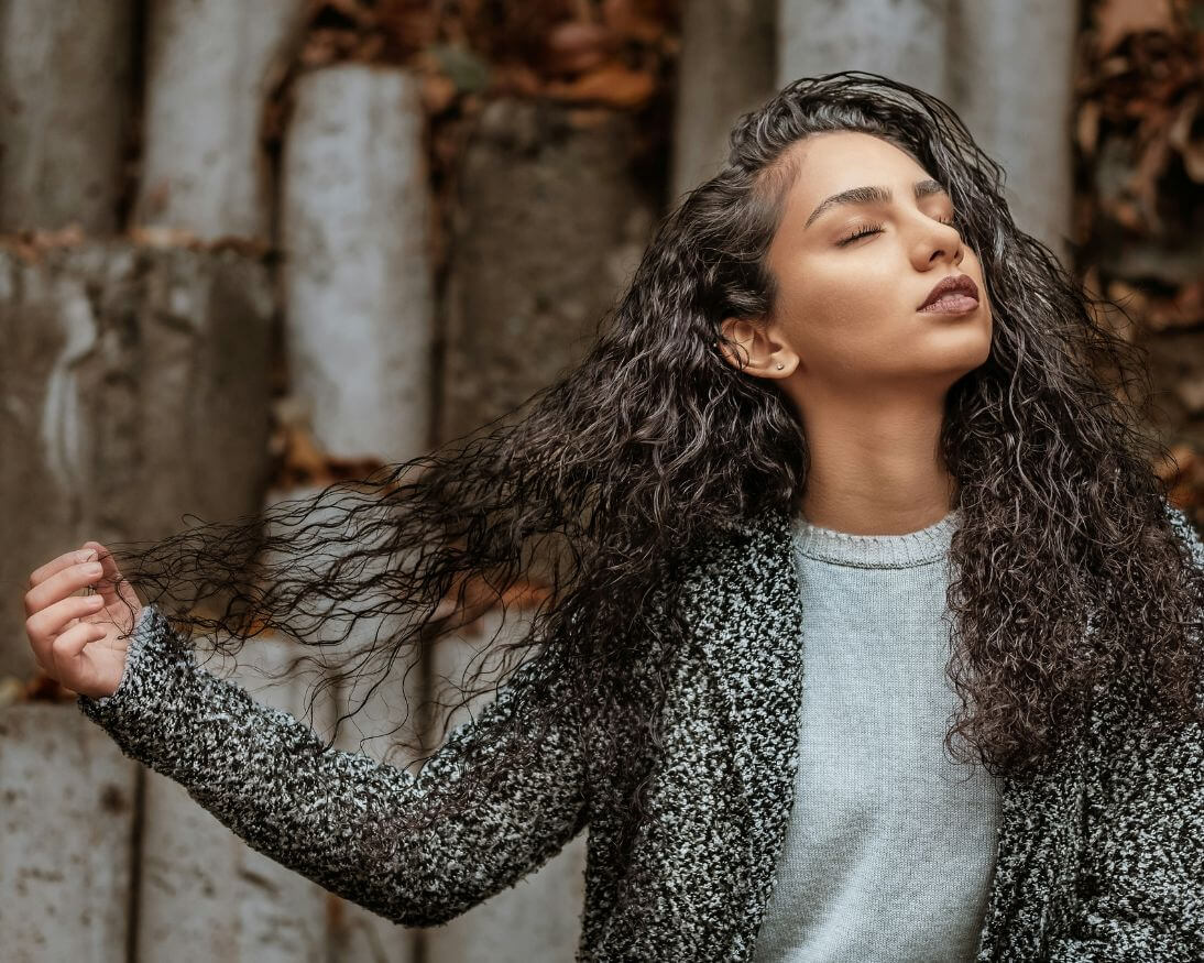 dark hair woman pulling her curly hair with eyes closed