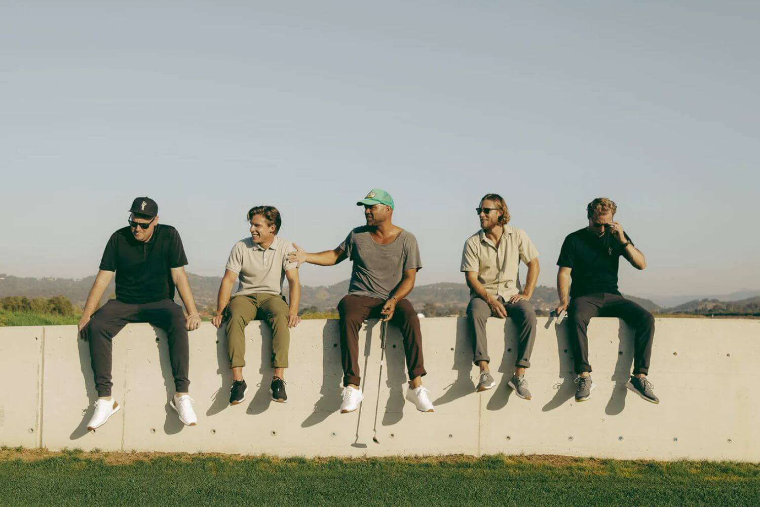 5 men sitting on wall from true golf team